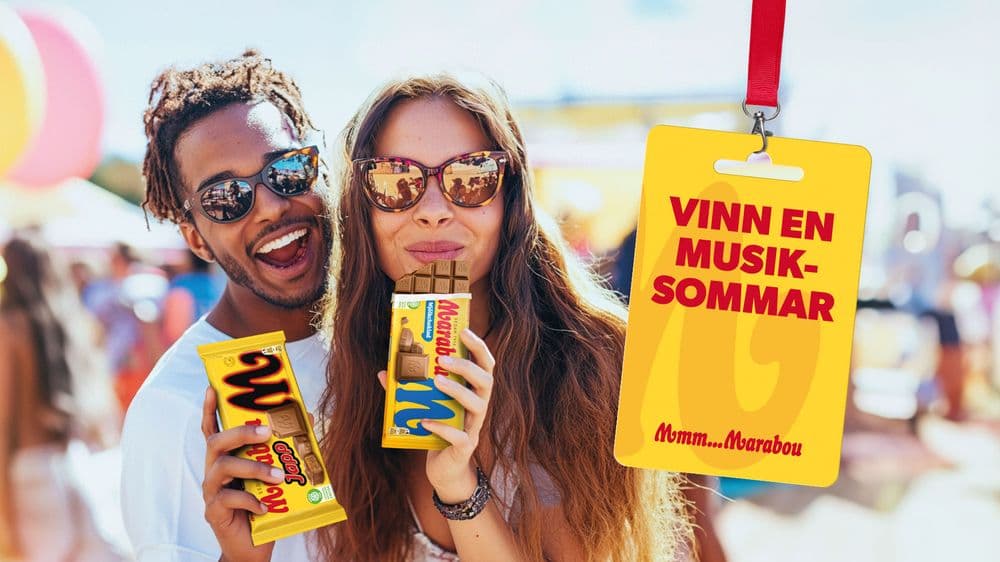 Ett leende par njuter av chokladkakor utomhus, med en skylt i förgrunden som lyder ‘Vinn en musik-sommar’.